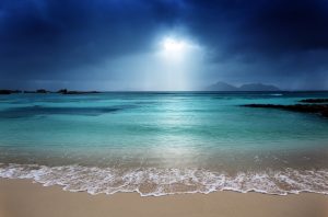A beach with sun shining through dark clouds