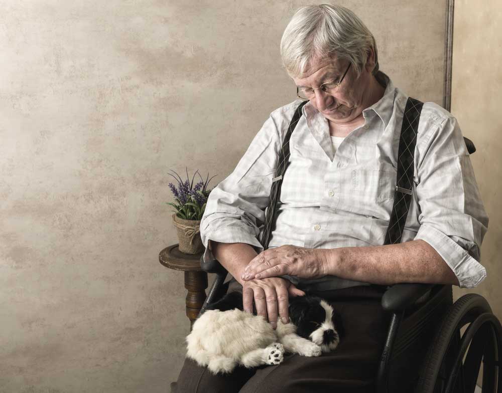Photo of elderly man sitting in a chair, holding a black and white puppy.