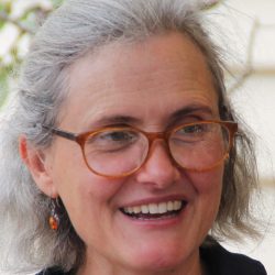 Headshot of Jane. Jane is smiling, has shoulder length silver hair and wears red glasses